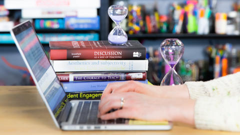 Hands typing on a MacBook laptop in front of colorful bookshelves.