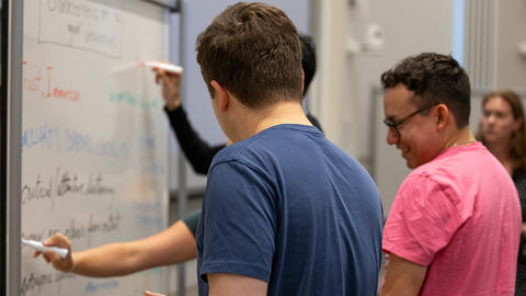 Three students writing at a whiteboard