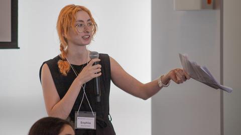 Teaching Development Fellow with microphone and paper in hand speaking at event
