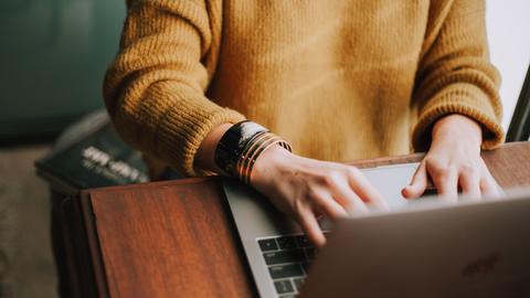 person in yellow sweater typing on macbook