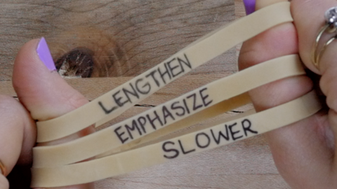 hands over table stretching out rubber bands with words "Lengthen," "Emphasize," and "Slower" written on them