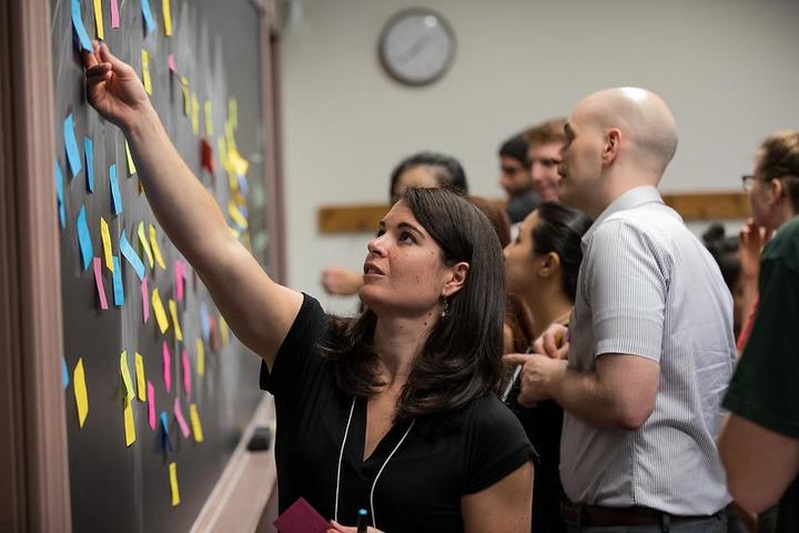 Lauren reaches for a sticky note on a blackboard at the Fall Teaching Conference.