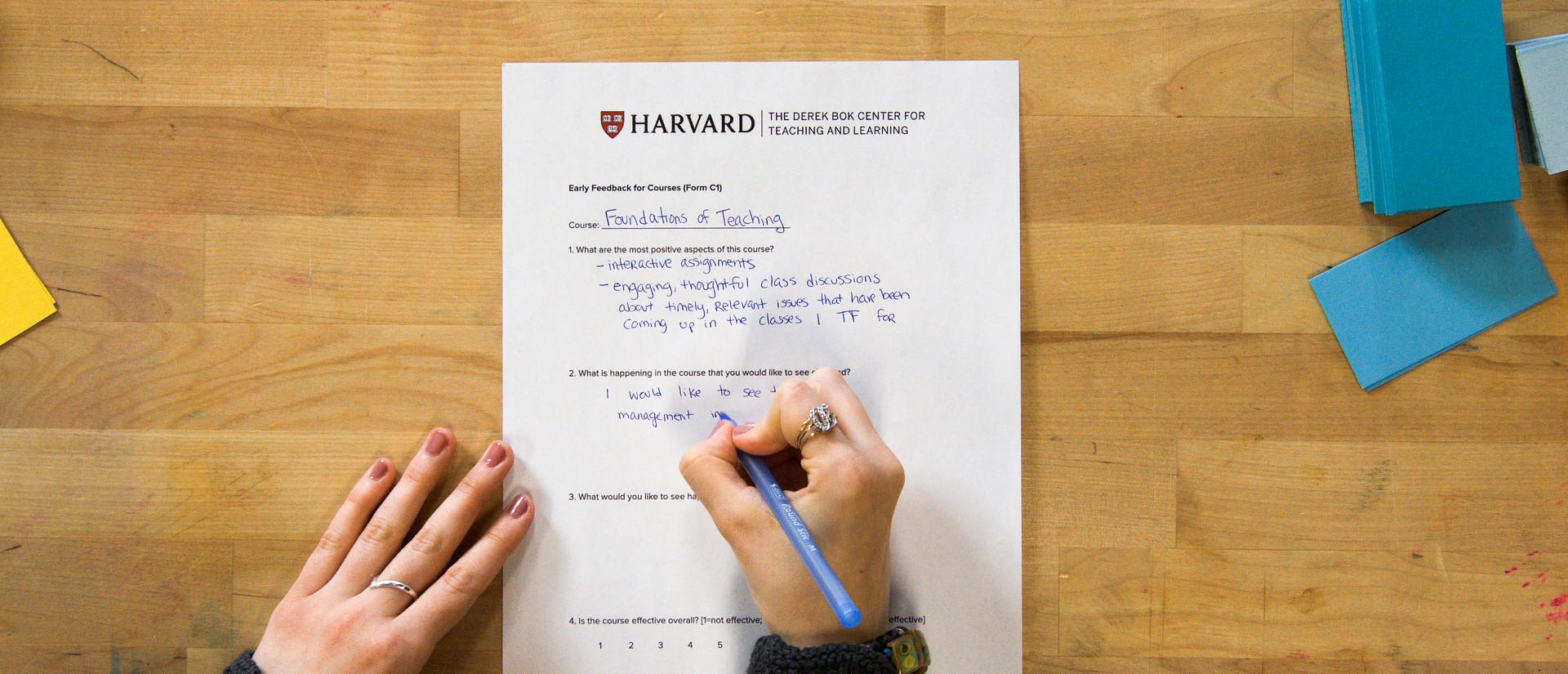 Overhead view of hands writing feedback on an evaluation form.