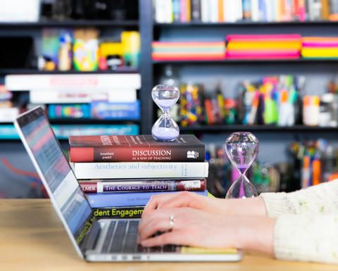 Hands typing on a MacBook laptop in front of colorful bookshelves.